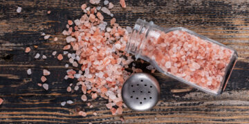 Himalayan salt coming out of open salt shaker on a dark wooden background top view - MAwebzine Himalayan salt coming out of open salt shaker on a dark wooden background top view