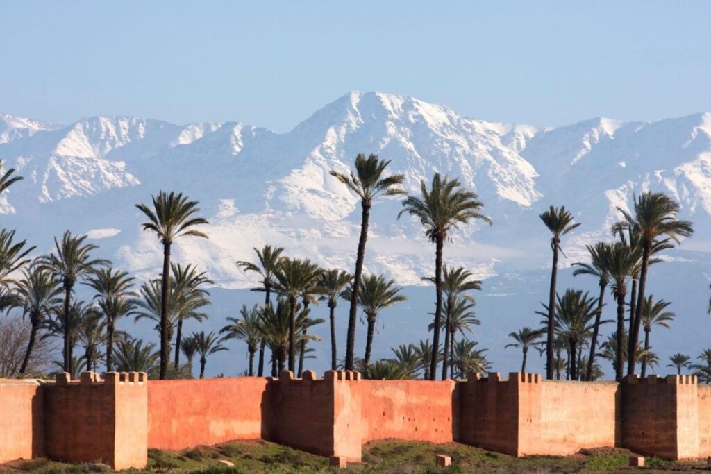 Snow-capped Atlas Mountains towering behind Marrakech cityscape during December winter getaway season, showcasing spectacular mountain views under clear blue Moroccan skies