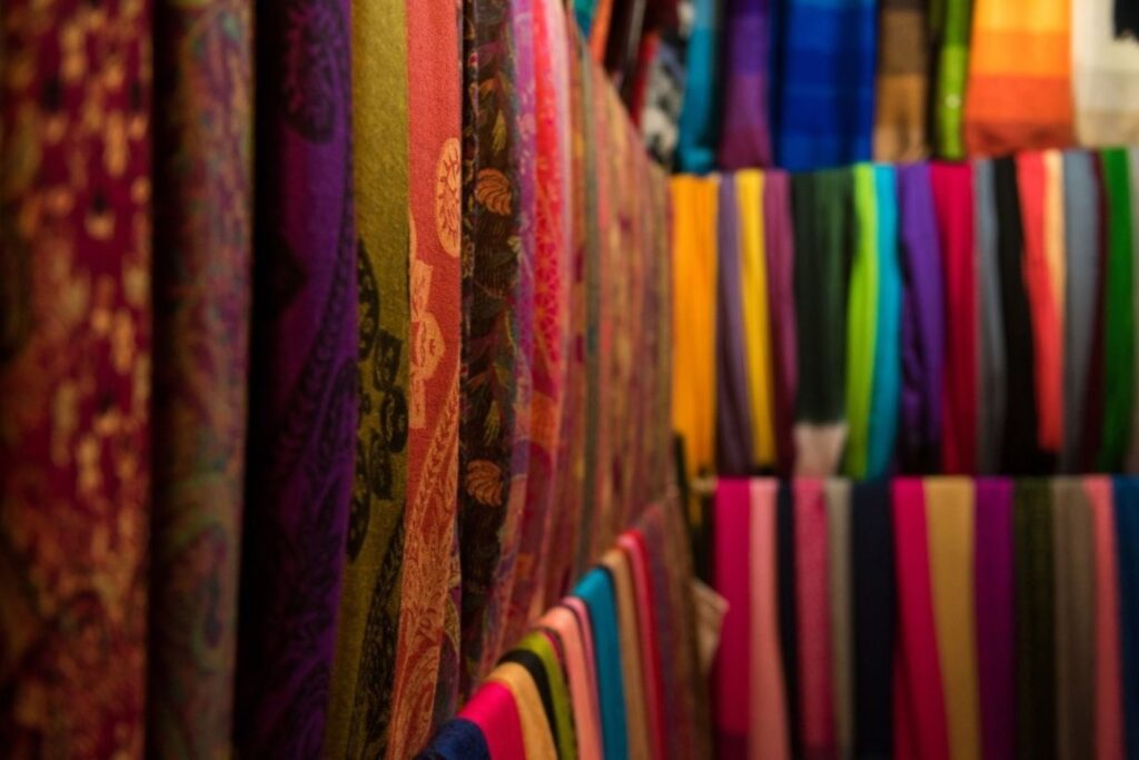 أوشحة ومنسوجات مغربية نابضة بالحياة منسوجة يدويًا معروضة في سوق تقليدي، مثالية لتغليف الهدايا الصديق للبيئة، تعرض براعة الحرفيين وبدائل الأقمشة المستدامة للورق القابل للتصرف