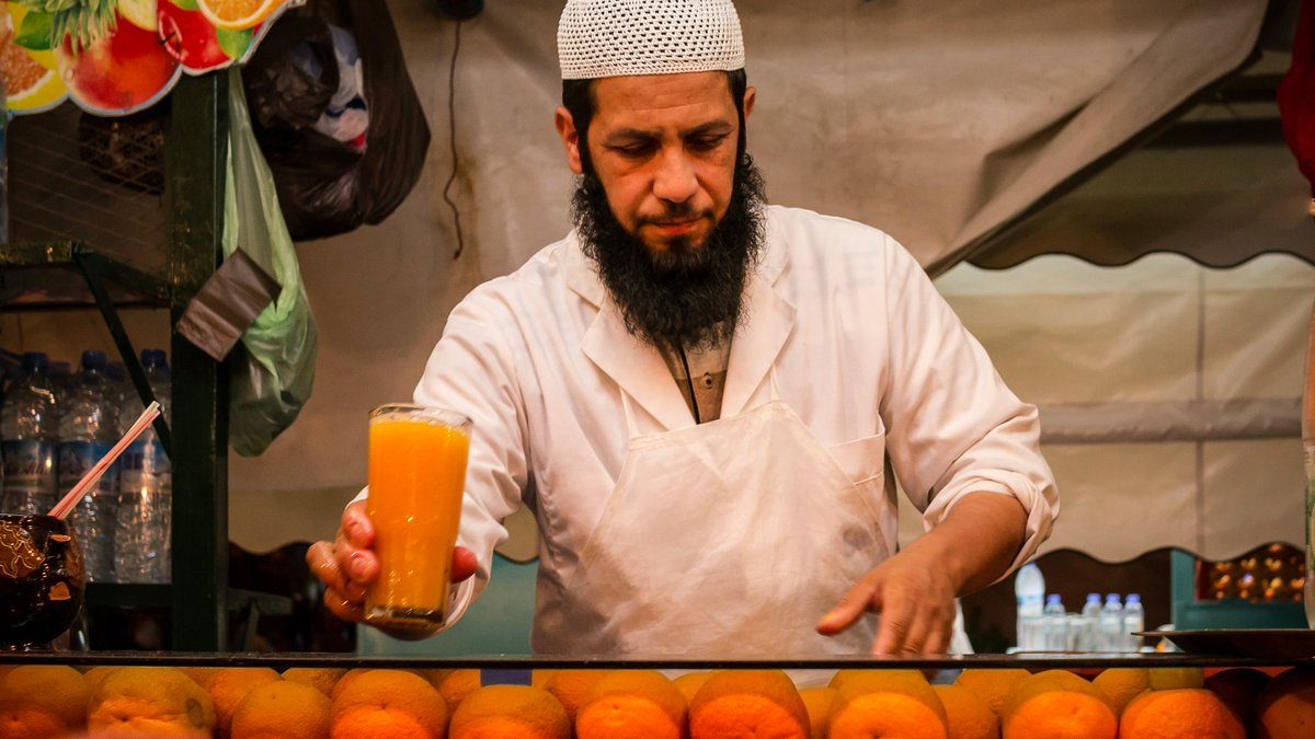 Een verkoper op een Marokkaanse marktstand die een glas verfrissend Marokkaans drankje aan een klant geeft op een hete zomerdag