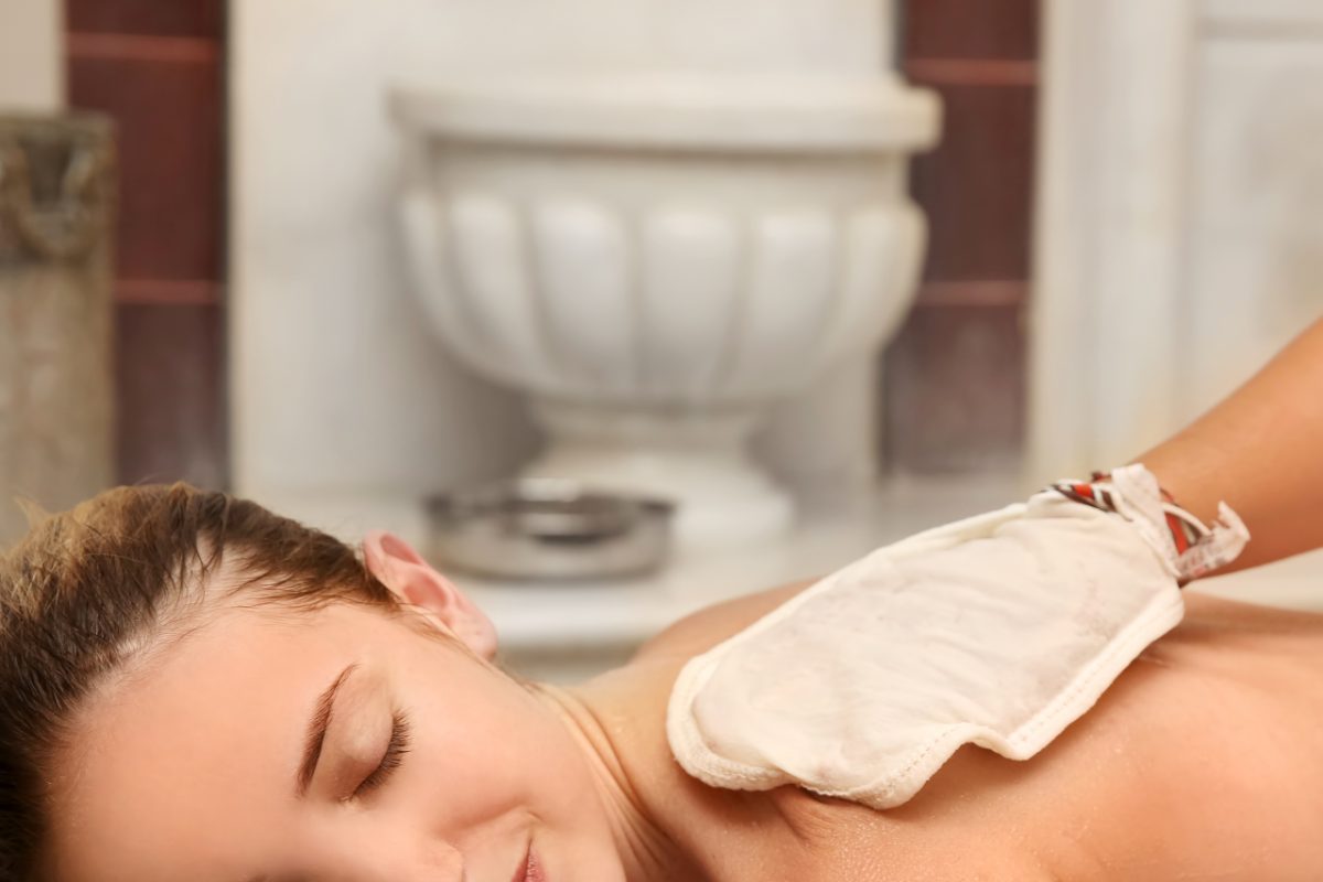 Een bekwame bediende voert hammam rituele exfoliatie uit met een kessa handschoen op een cliënt in een Marokkaanse wellness ruimte.