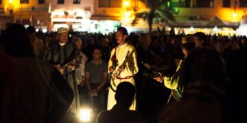 a-maalem-musician-performing-at-the-morocco-festival-unsplash - MAwebzine Een maalem-muzikant optredend tijdens het festivalseizoen van Marokko in Essaouira, met een menigte rond het open-air podium