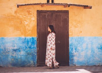 Een Marokkaanse vrouw in een vloeiende linnen kaftan bladert door een medinamarkt, die duurzame mode in Marokko vertegenwoordigt