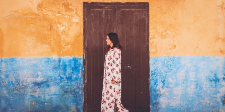 Een Marokkaanse vrouw in een vloeiende linnen kaftan bladert door een medinamarkt, die duurzame mode in Marokko vertegenwoordigt