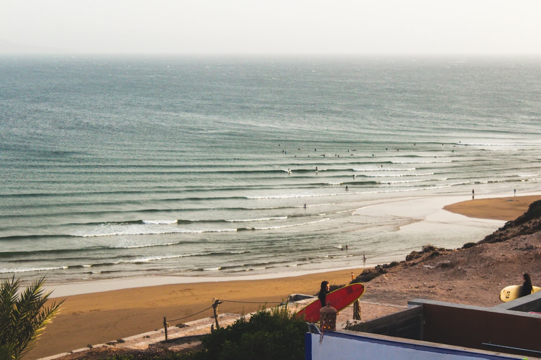 Een surfer draagt een bord door een Marokkaans dorp na een ochtendseSSie, wat het leven laat zien wanneer surfen in Marokko in de zomer