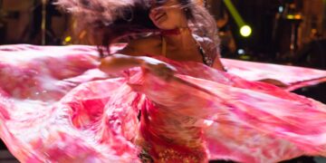 buikdans-outfit-unsplash - MAwebzine Een uitvoerder in traditioneel kostuum op het podium op het populair kunstfestival in Marrakech, omringd door een menigte 's nachts
