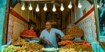 kopen-straatvoedsel-marokko-medina-unsplash - MAwebzine Een vrouw die Marokkaans straatvoedsel kiest bij een druk kraampje in de medina, een scène die de dagelijkse vreugde van veilig eten in Marokko vastlegt