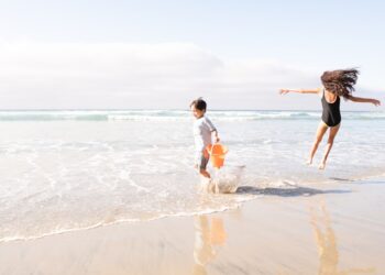 Een moeder en haar kinderen die kinderen koel houden op een zonnig Marokkaans Atlantisch strand, sprietend in ondiep water dicht bij de kust.
