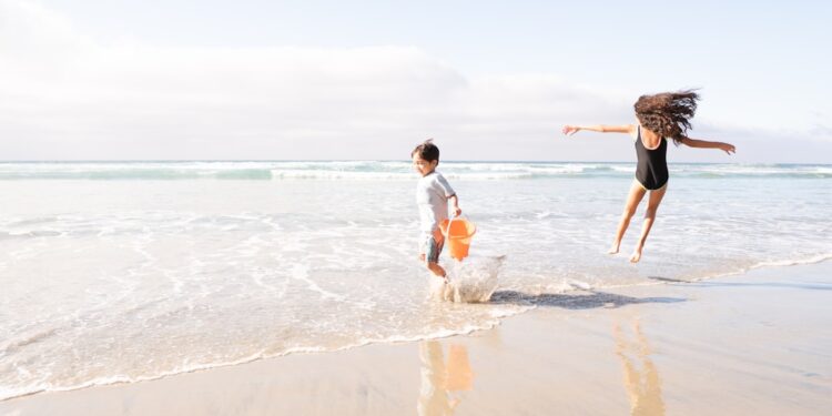 Een moeder en haar kinderen die kinderen koel houden op een zonnig Marokkaans Atlantisch strand, sprietend in ondiep water dicht bij de kust.