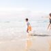 children-playing-beach-unsplash - MAwebzine Een moeder en haar kinderen die kinderen koel houden op een zonnig Marokkaans Atlantisch strand, sprietend in ondiep water dicht bij de kust.