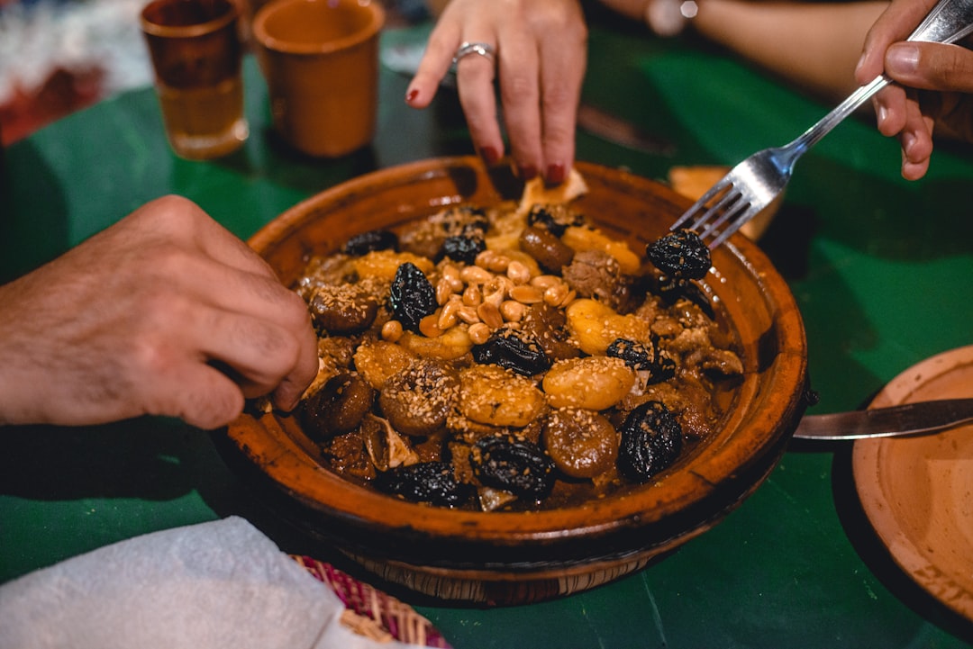 Een man scheurt Marokkaans brood om op te scheppen uit een dampen de Marokkaanse tajine die in een aarden pot op tafel wordt geserveerd.