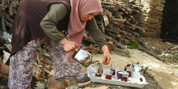 man-pouring-moroccan-tea-pexels - MAwebzine Een vrouw in traditionele klederdracht schenkt Marokkaanse muntthee uit een zilveren theepot op een sierlijk koperen blad in een rijadbinnenplaats