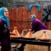 moroccan-woman-serving-tagine-pexels - MAwebzine Een Marokkaanse vrouw tilt het deksel van een aarden Marokkaanse tajine op aan een familietafel in een traditionele riadkeuken.