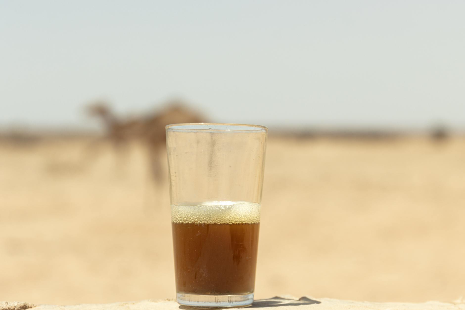 Een reiziger houdt een klein glaasje Marokkaanse muntthee vast in een Saharakamp terwijl een Berber-gids de volgende ronde voorbereidt