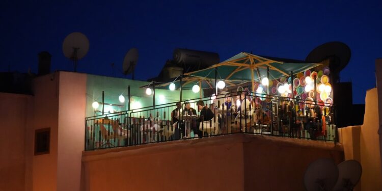 woman-drinking-cocktail-rooftop-marrakech-unsplash - MAwebzine genieten van cocktails op een van de dakterrassen in Marrakech, met de moskee van Koutoubia op de achtergrond bij zonsondergang.