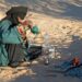 woman-pouring-moroccan-mint-tea-unsplash - MAwebzine Een vrouw die het traditionele hoge-giet-ritueel van Marokkaanse dranken uitvoert, die atay in kleine glazen serveert in een zonnige binnenplaats