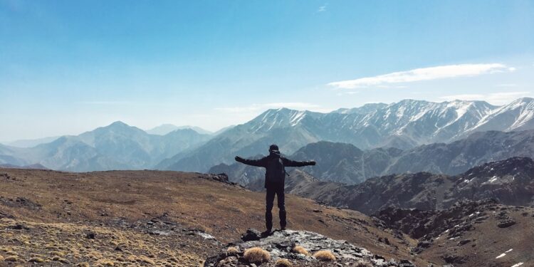 hiker-atlas-mountains-morocco-morning-unsplash - MAwebzine Un randonneur marche sur un sentier de montagne près d'Azilal au lever du soleil avec les pics du Haut Atlas en arrière-plan