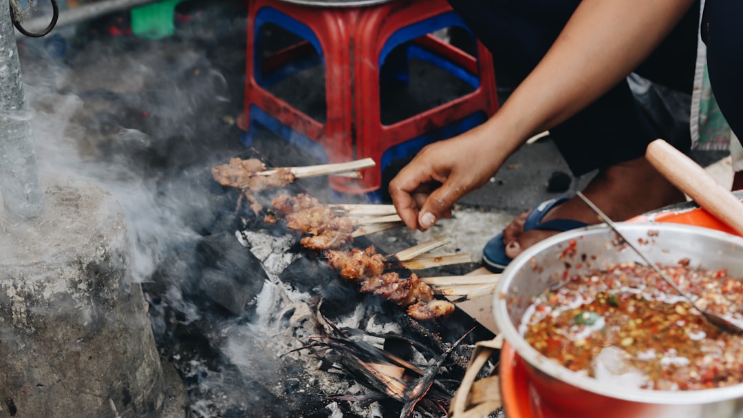 A Moroccan family gathered around a charcoal grill for a summer cooking session, making kefta skewers in a courtyard