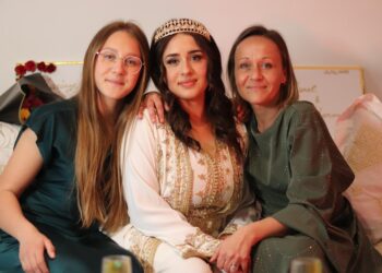 A Moroccan family dressed in traditional djellabas gathering outdoors during Fête du Trône festivities in a city medina