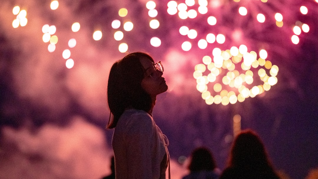 A woman in the crowd watching fireworks light up the sky above a Moroccan city during Fête du Trône