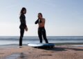 surf-instructor-teaching-beginner-on-beach-unsplash - MAwebzine A certified coach at one of Morocco's surf schools helps a beginner stand on a board for the first time on the Atlantic coast