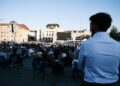 A Moroccan man in a crowd watches a public screen during the Throne Day national address in Morocco