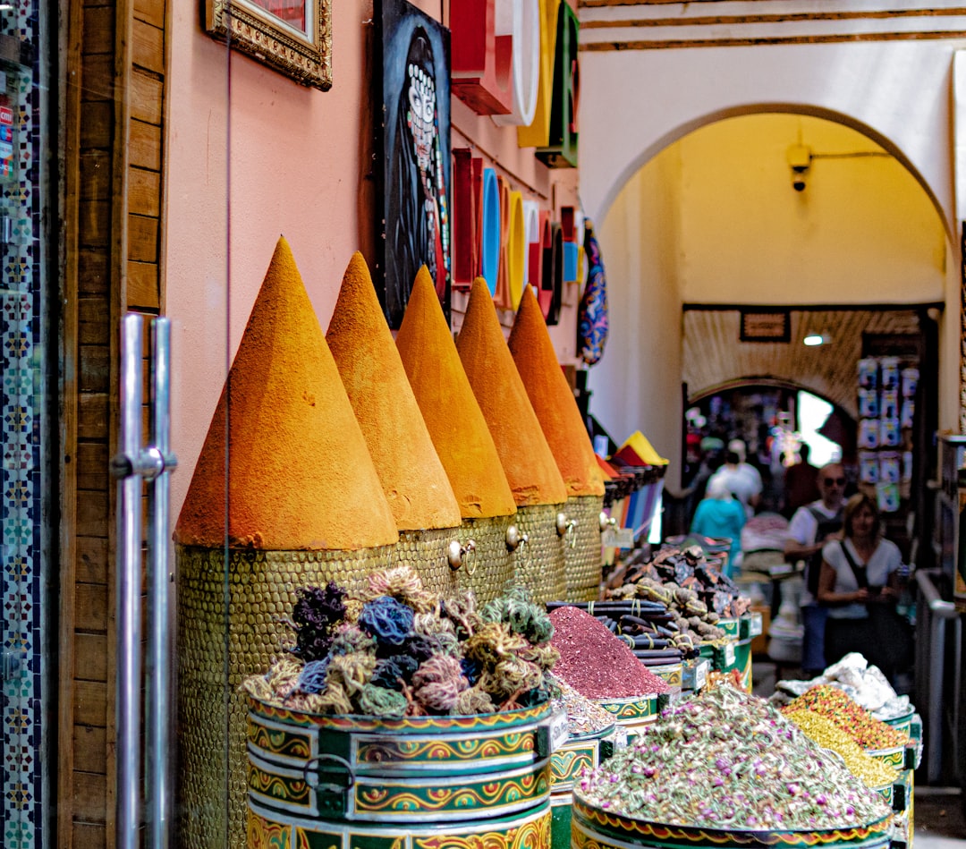 A vendor arranges colorful spices at a stall in Moroccan markets, where a customer holds a reusable cloth bag.