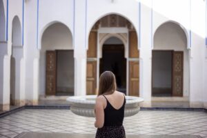 A woman sitting beside a central courtyard fountain in a traditional Moroccan riad, experiencing natural riad cooling.