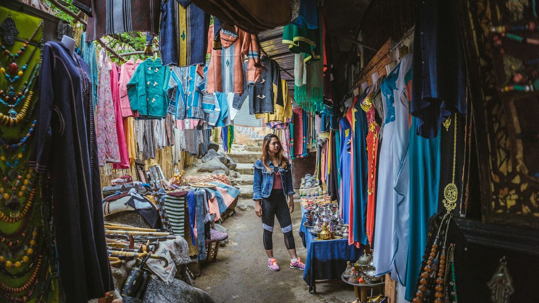 A woman selecting handcrafted garments in a Moroccan medina market, exploring cooperative textile pieces